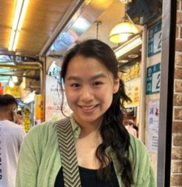 Photo of a smiling young woman with a curly black hair ponytail in a shop in a light green shirt.