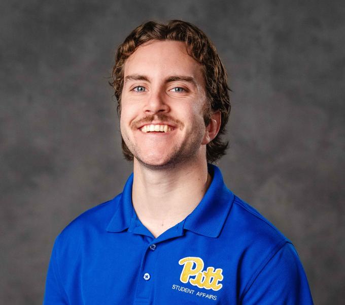 Headshot of a smiling man with short, wavy blonde hair and a mustache, wearing a University of Pittsburgh polo shirt.