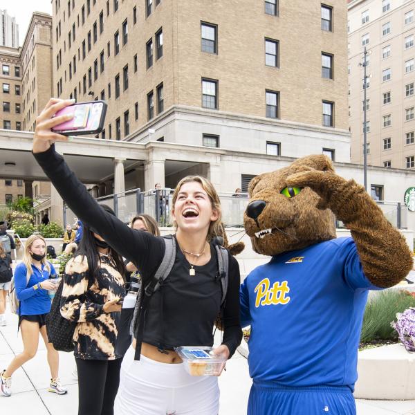 A female student with blonde hair in a black long sleeve top taking a selfie with Roc the Panther.