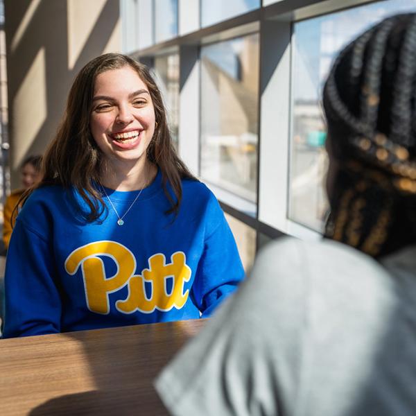 Woman with brown hair in a blue crewneck sweatshirt with yellow Pitt script.