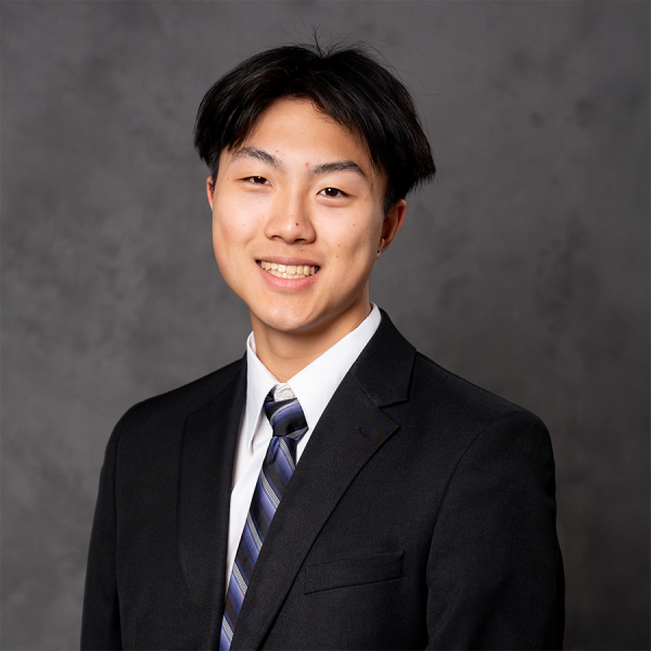 A man with short dark hair smiling in a black suit.