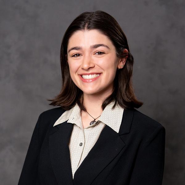 A woman with short dark hair smiling in a black blazer over a white button down top.