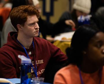 A male student in a red hoodie seated at a table with a blue tablecloth.