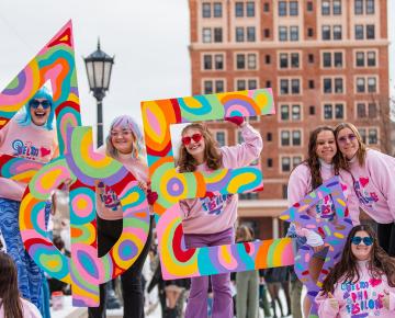Students in pick sweatshirts holding large Greek letters.