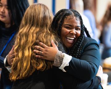 Two female students wearing suits and hugging.