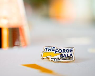 An enamel pin that reads "The Forge Gala" on a white tablecloth.