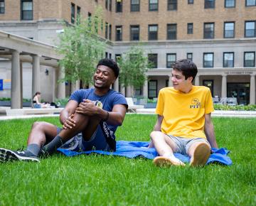 Two students sitting in the grass on a sunny day.