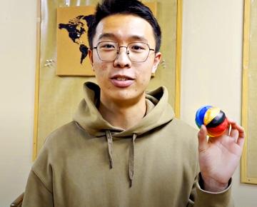 Male student looking into camera holding a colorful clementine-shaped object.