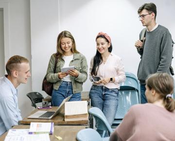 A group of young students smile as they look at photos and pieces of paper.