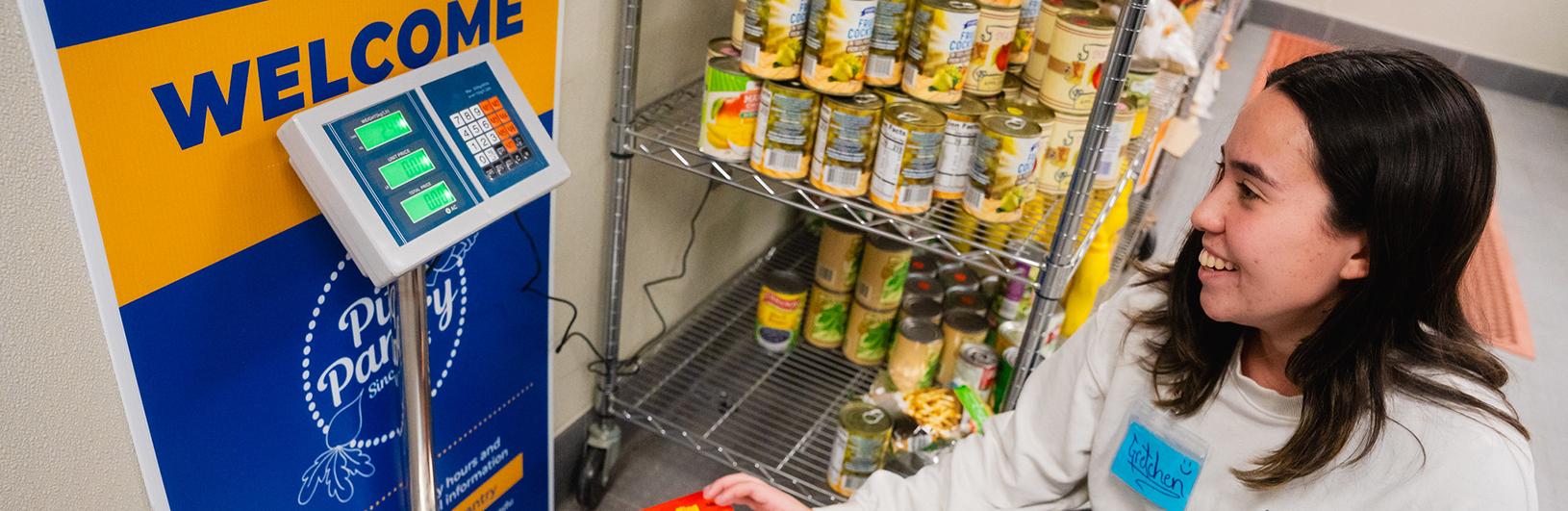 A woman in a white shirt with dark hair smiling and weighing food at the Pitt Pantry.