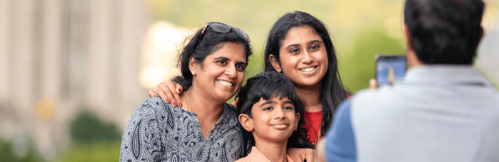 Three smiling family members pose for a photo being taken by another person.