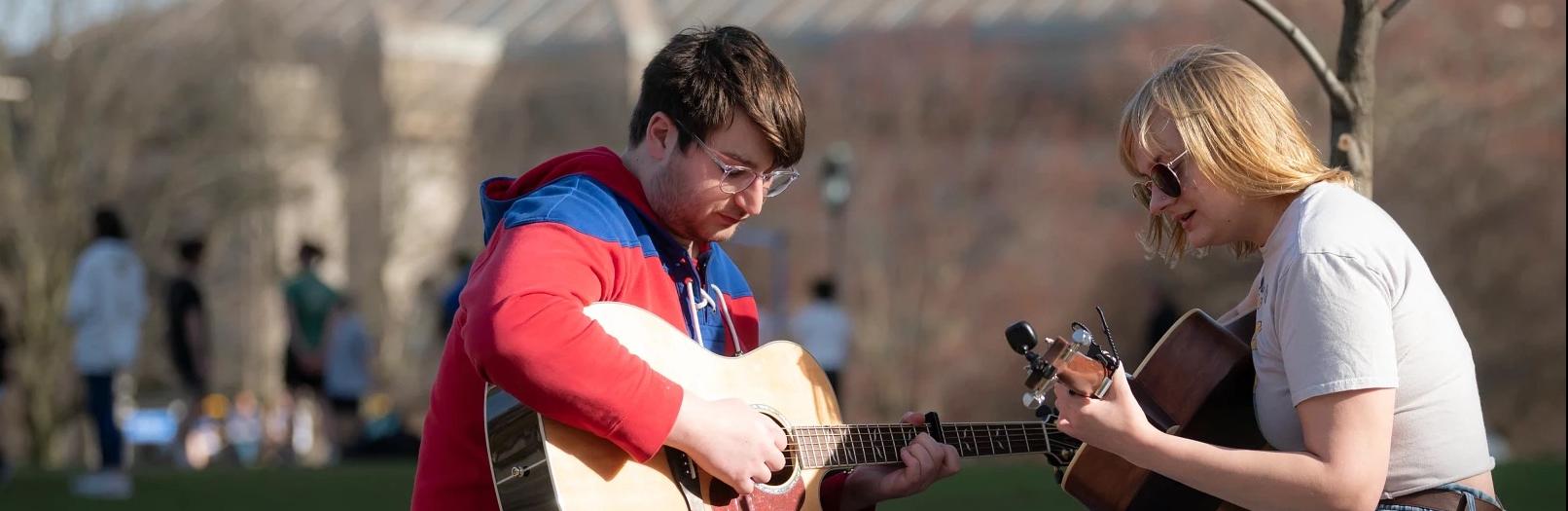 Two people playing guitars outdoors.