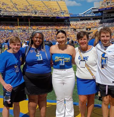 Five people dressed in Pitt gear standing on the Acrisure Stadium field.