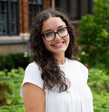 A woman with long dark hair in a white top smiling with glasses on.