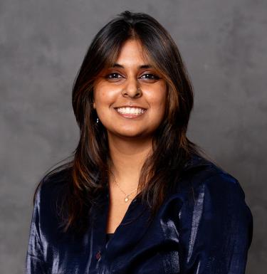 A woman with long dark hair smiling in a blue velvet top.