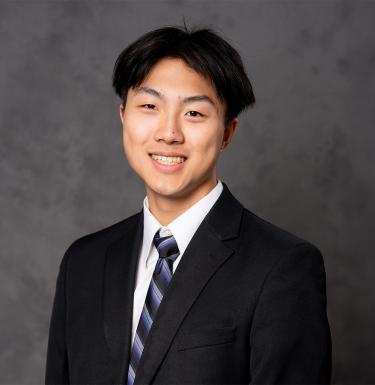 A man with short dark hair smiling in a black suit.