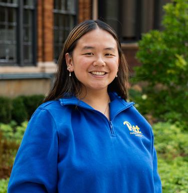 A woman with long dark hair smiling in a blue quarter zip.