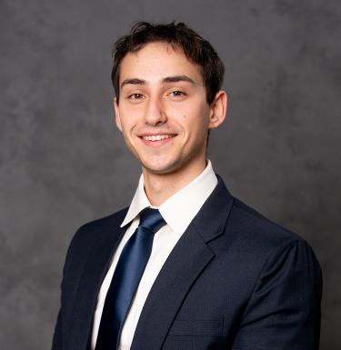 A man with short dark hair smiling in a navy suit.