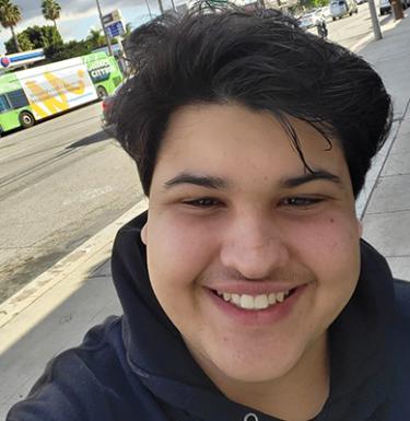 A man with short dark hair smiling in a black hoodie.