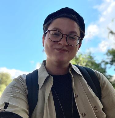 Selfie of a smiling person outside with glasses and short hair.