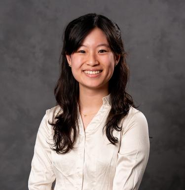 A woman with long dark hair smiling in a white button down blouse.