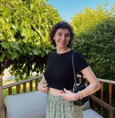 Outdoor photo of a smiling woman with short, dark hair in a green floral skirt and black crop top.