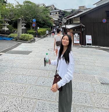 A woman with long dark hair in a long sleeve white top and green pants.