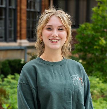 A woman with curly blonde hair smiling in a green top.