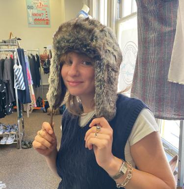 Photo of a smiling blonde young woman wearing an eared furry hat in a thrift store.