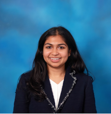 Headshot of a smiling young woman in a glittery black blazer and white shirt on a blue background.