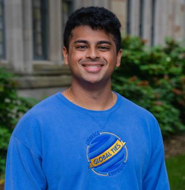 Outdoor headshot of a smiling man in a blue Global Ties crewneck shirt.