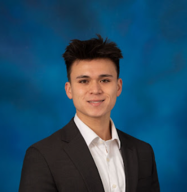 Headshot of a smiling young man in a suit on a blue background.