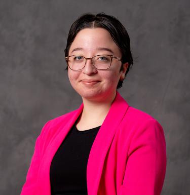 A woman with short dark hair and glasses smiling in a pink blazer.