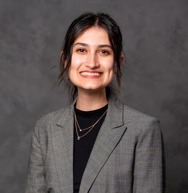 A woman with dark hair smiling in a grey blazer over a black top.
