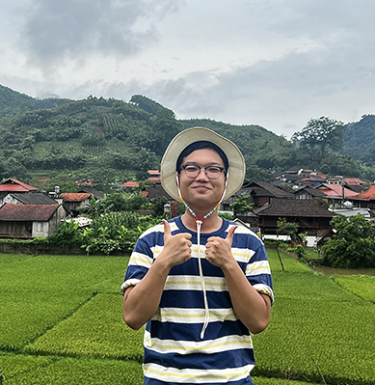 A man in a straw hat and striped tshirt standing in front of a meadow