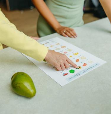 Two people point at a nutrition print out on a table next to a green pear.