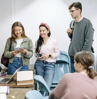 Four young students stand around discussing papers.