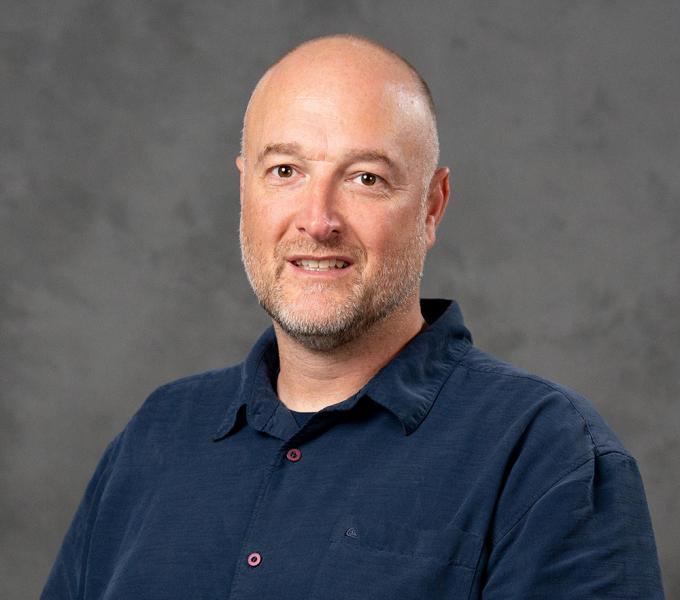 Photo of a man smiling in front of a grey background.