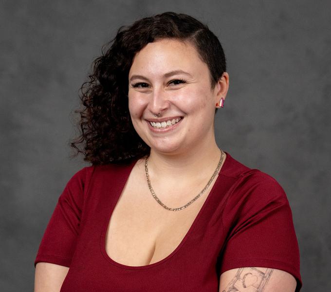Headshot of a smiling brunette woman in a dark red blouse and necklace.