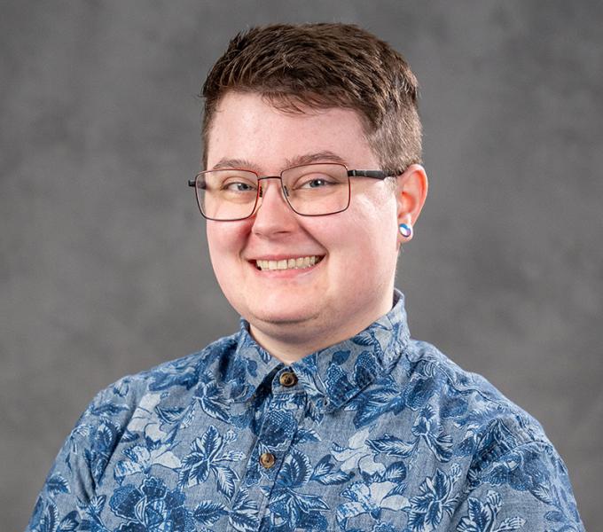 Person with short dark hair and glasses in a blue floral button down shirt.
