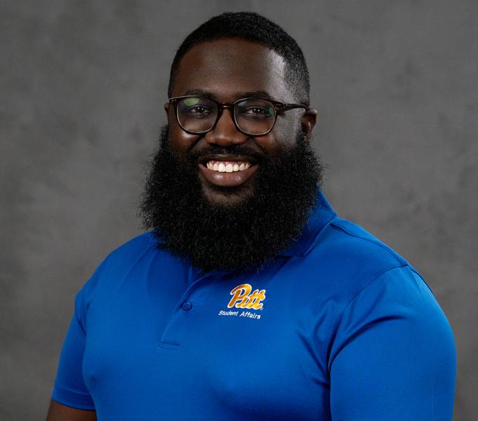 A man in a blue polo shirt smiling in front of a grey background.