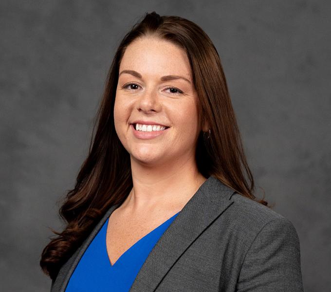 Woman in blue blouse and grey blazer with long dark hair.