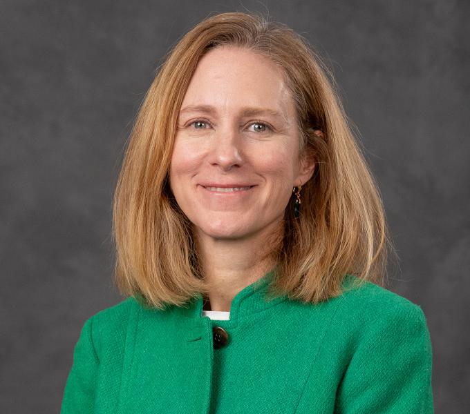 A white woman with short blonde hair smiling in a green blazer.