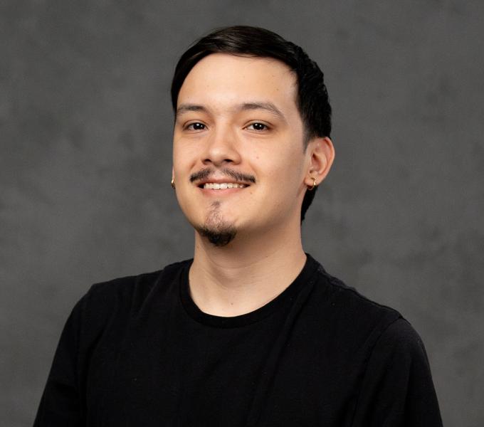Photo of a man with dark hair and dark facial hair in a black tshirt.