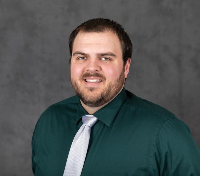 Headshot of a man in an emerald green button down shirt and silver tie.