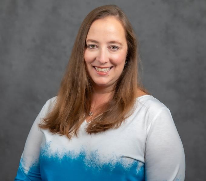 Headshot of smiling woman with long light brown hair and a white to blue ombre shirt.