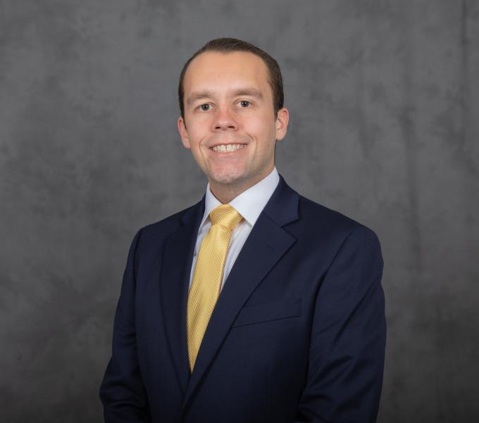 Headshot of smiling man in navy blue blazer and pale gold tie.