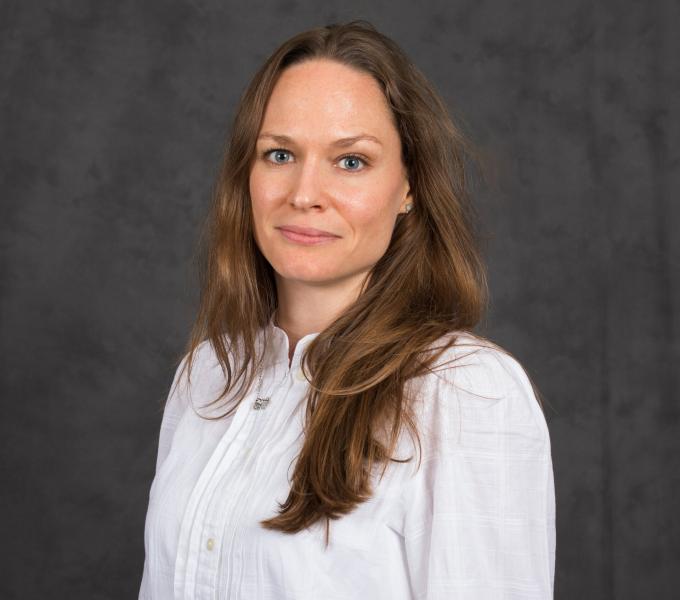 Headshot of woman with long wavy light brown hair in a white long-sleeved shirt.