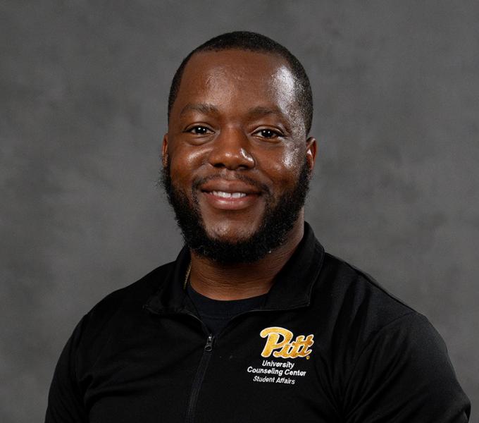 Photo of a man smiling in a black polo.