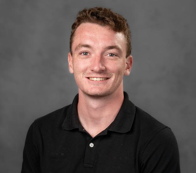 Headshot of a smiling young man in a black polo shirt.